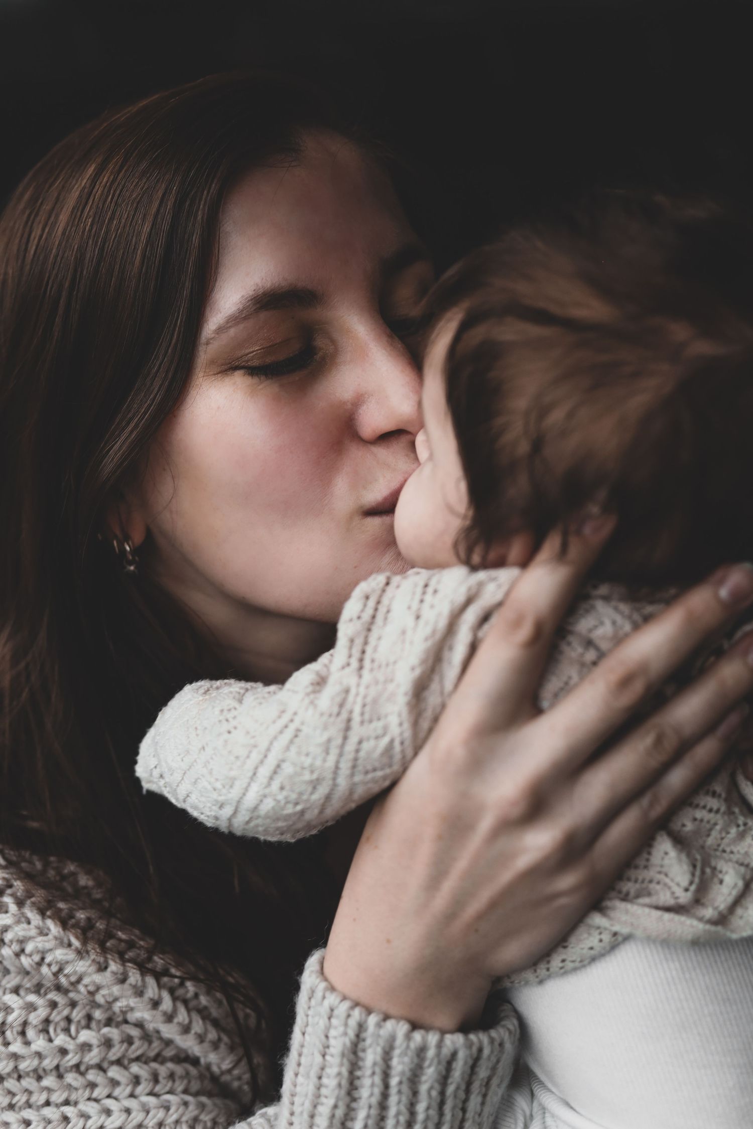 Mother tenderly kissing her newborn baby while wearing a cozy knit sweater.
