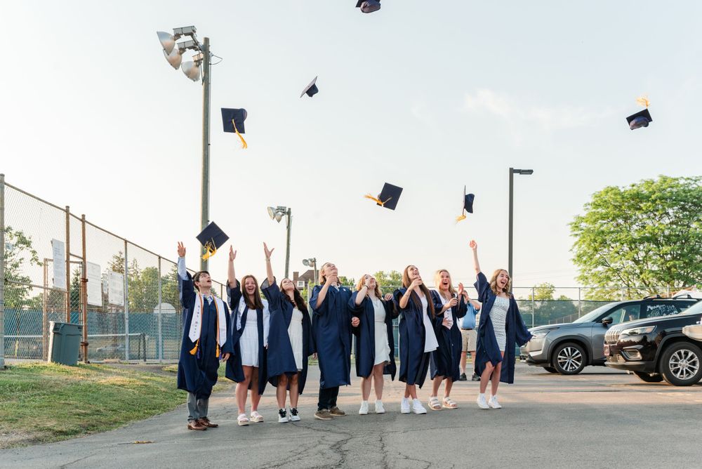 Graduating class in navy caps and gowns toss their mortarboards during celebration photo.