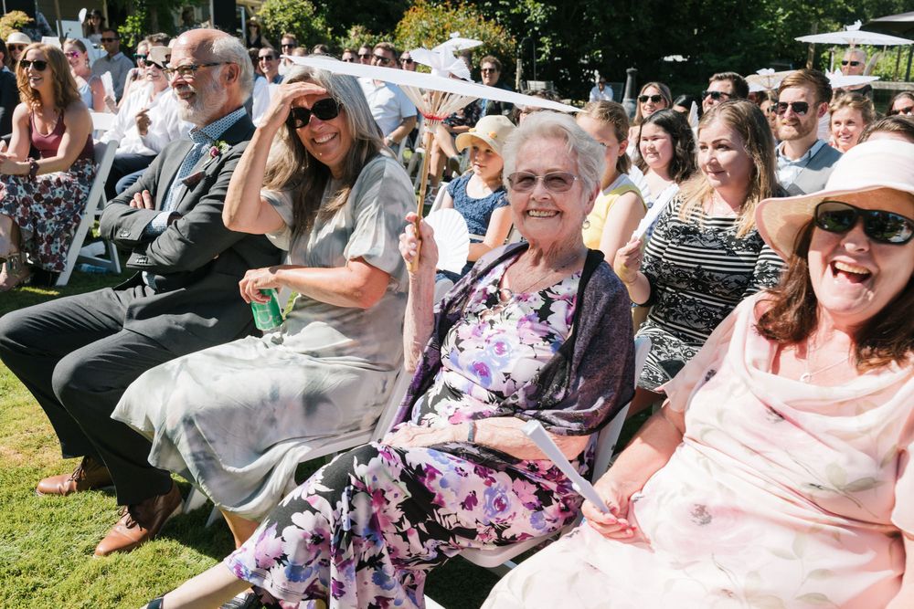 Family laugh under parasols to shield from the sun on Emery and Matt's hot summer wedding day in Victoria