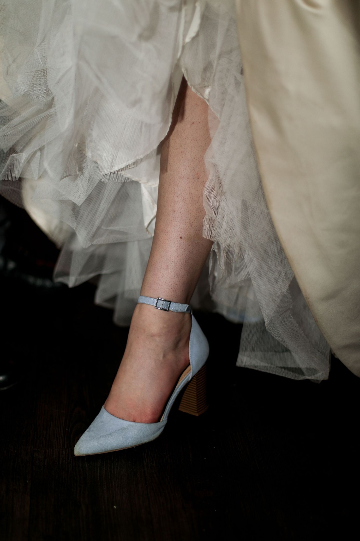 Light blue ankle-strap heel worn by bride against layers of white tulle.