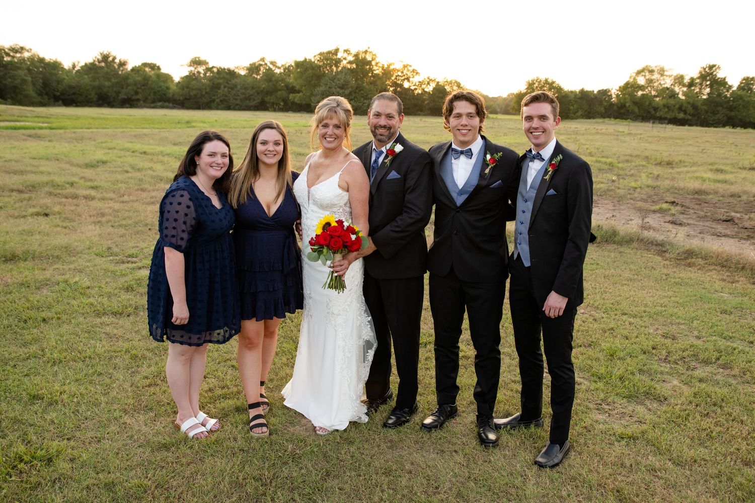A wedding party poses together outdoors at sunset.