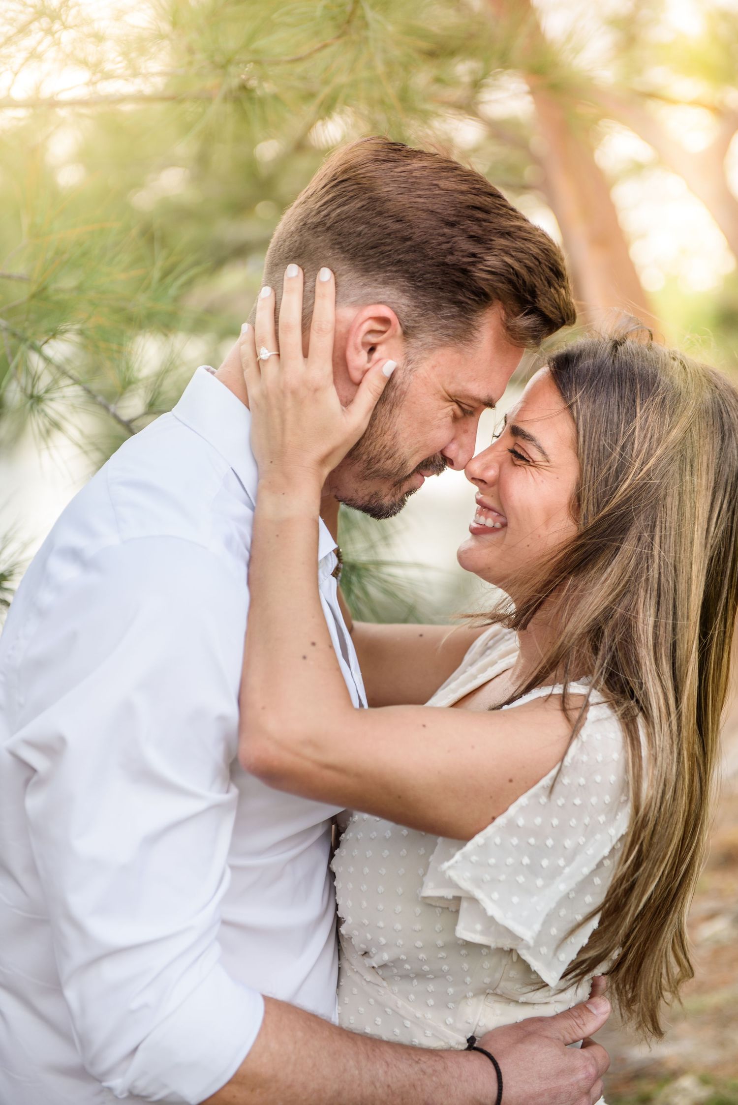 A couple shares an intimate moment outdoors, embracing and touching foreheads with genuine joy and affection.