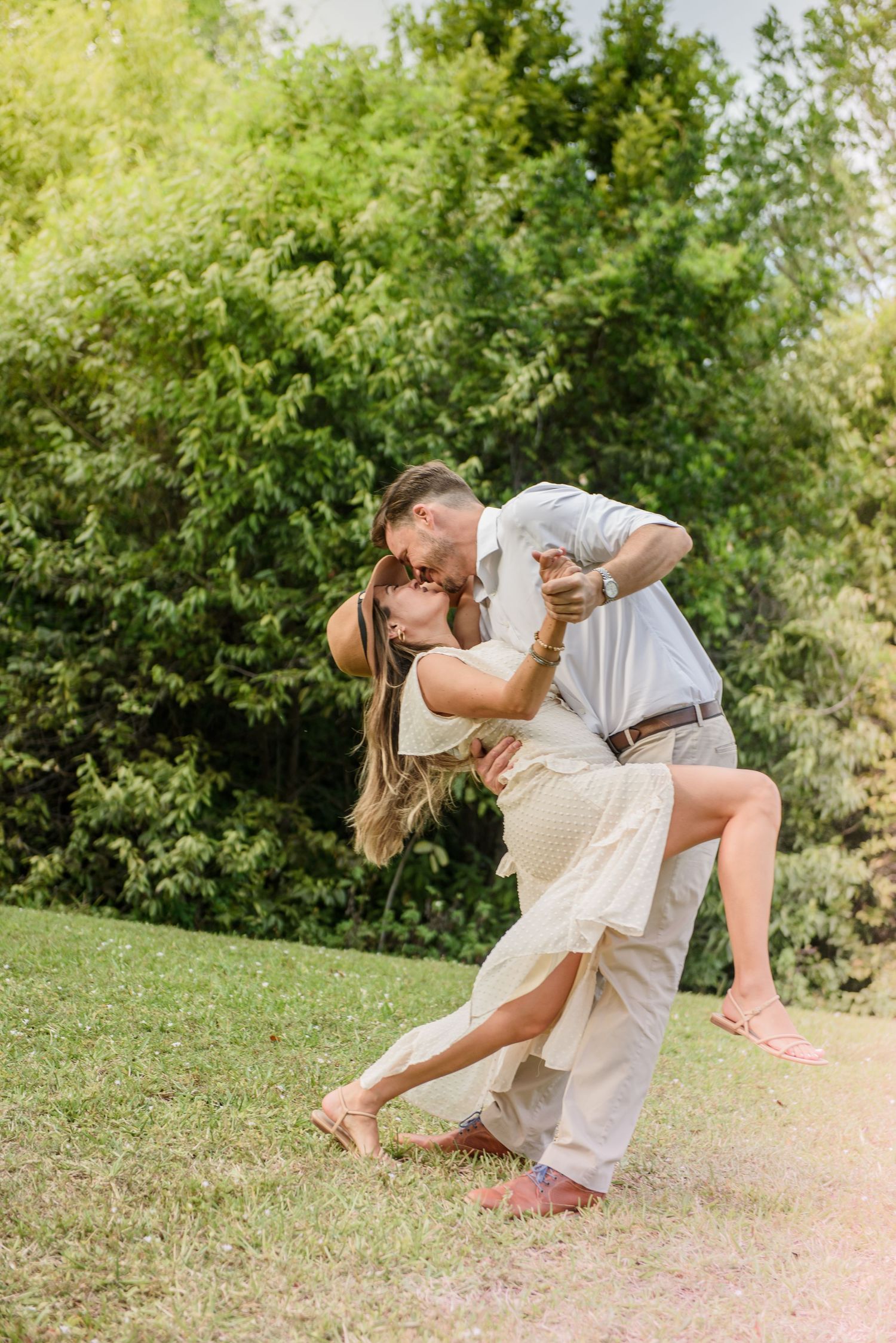 A couple performs a romantic dance dip on grass in a garden setting.