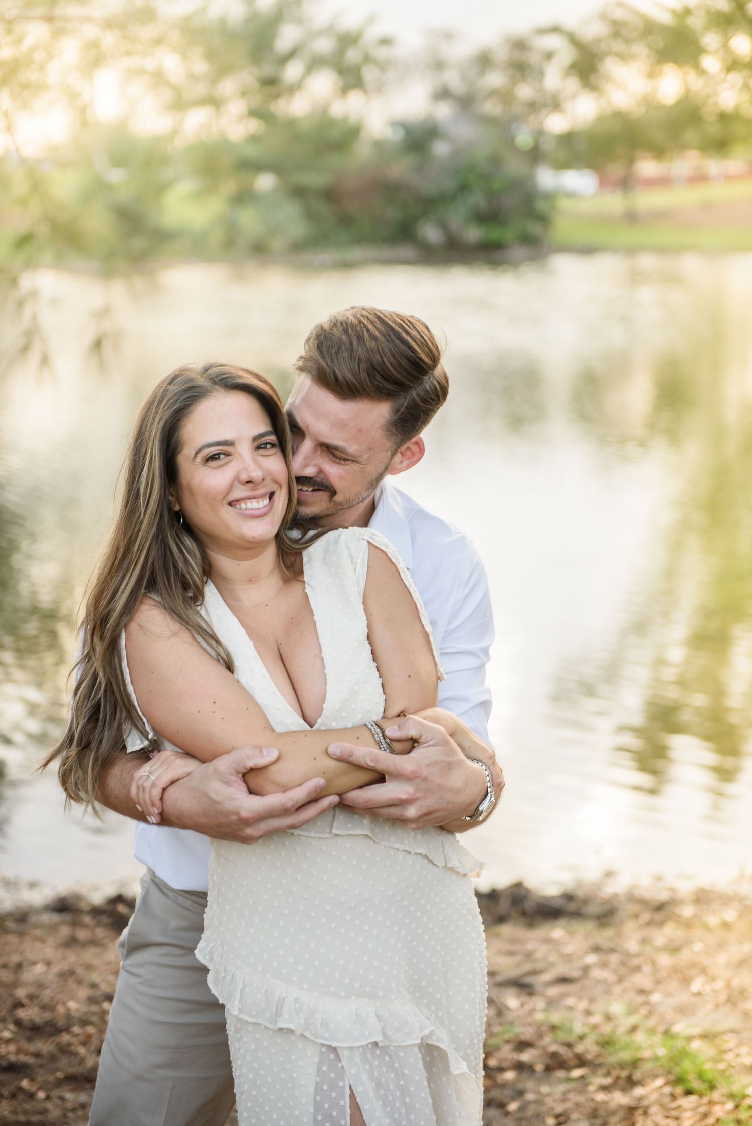 A romantic couple shares an intimate embrace by a tranquil lake during a sunset photoshoot in nature.