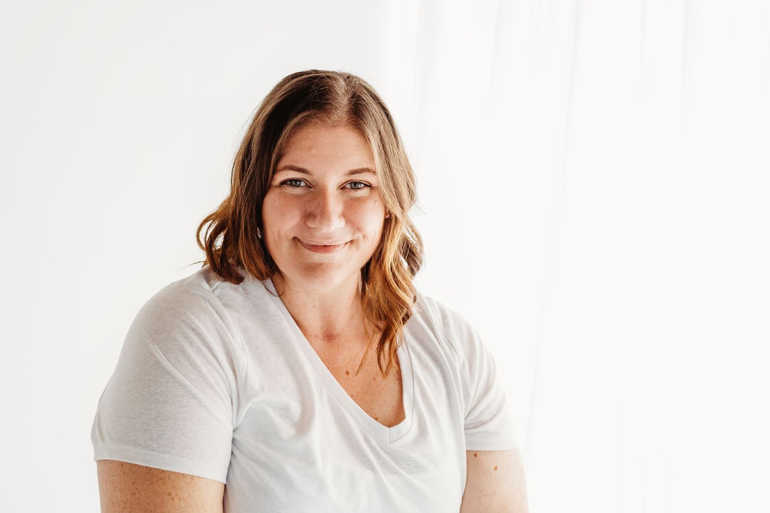 Woman wearing a white flowy dress poses against a light background in a studio setting.
