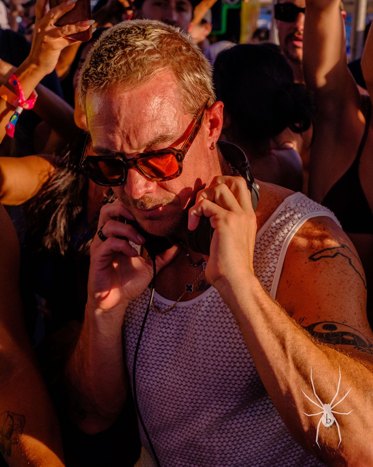 Concert attendee in tank top and sunglasses using phone in a crowded nighttime venue.