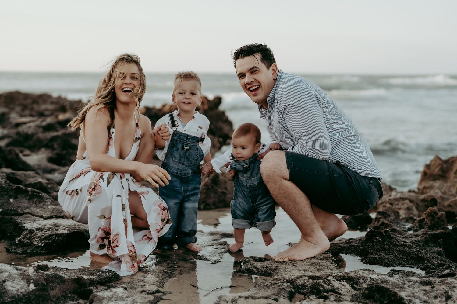 Family enjoying playful moments together on rocky beach at sunset.