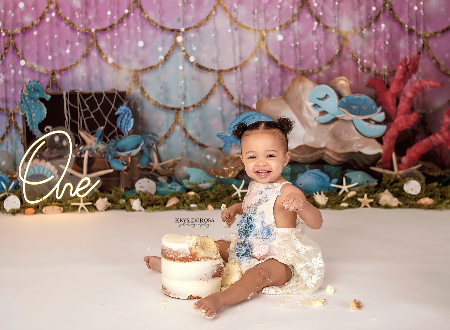 First birthday cake smash with mermaid scale backdrop and twinkling lights.