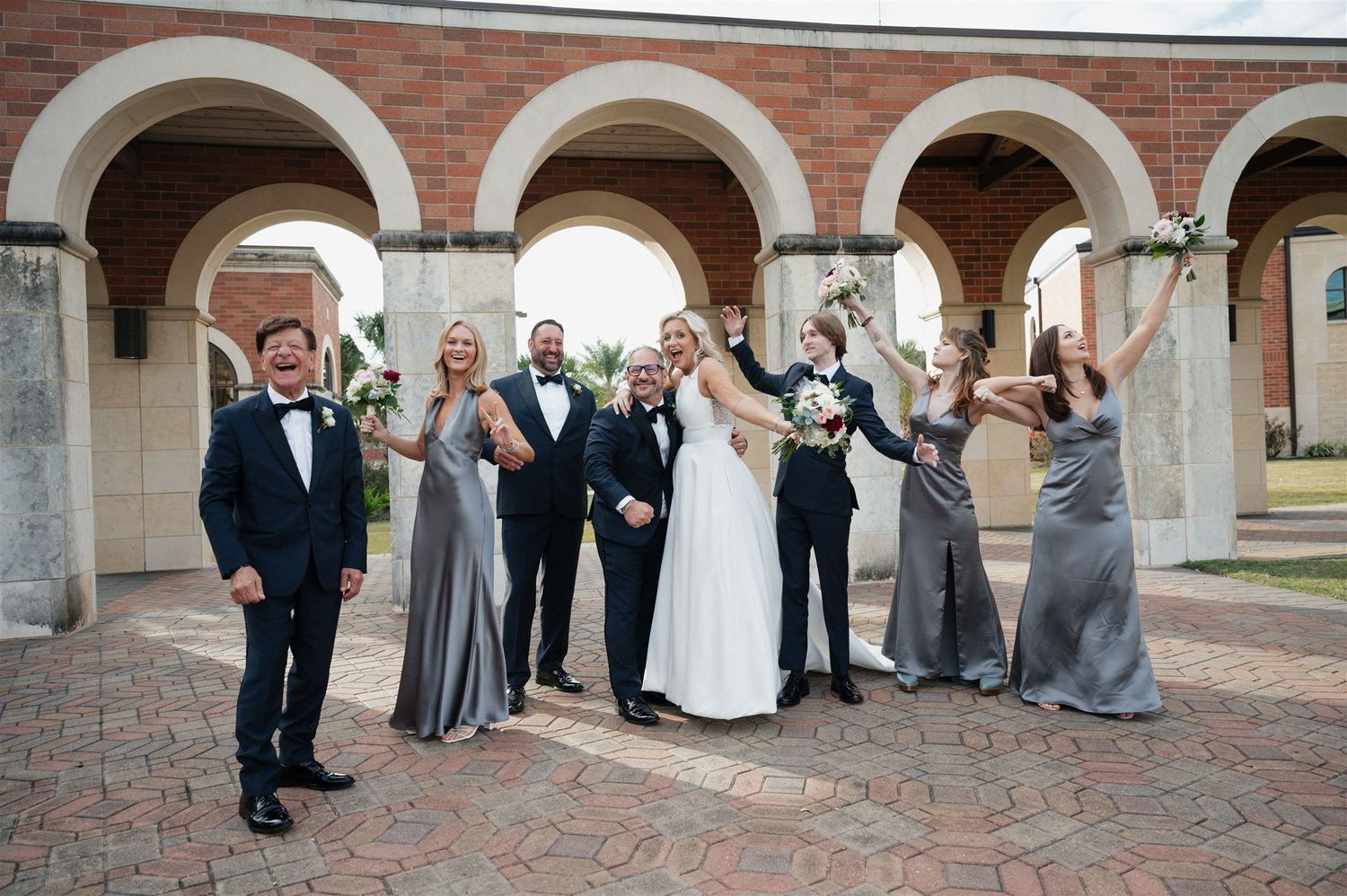 Wedding party celebrates joyfully under historic brick archways.