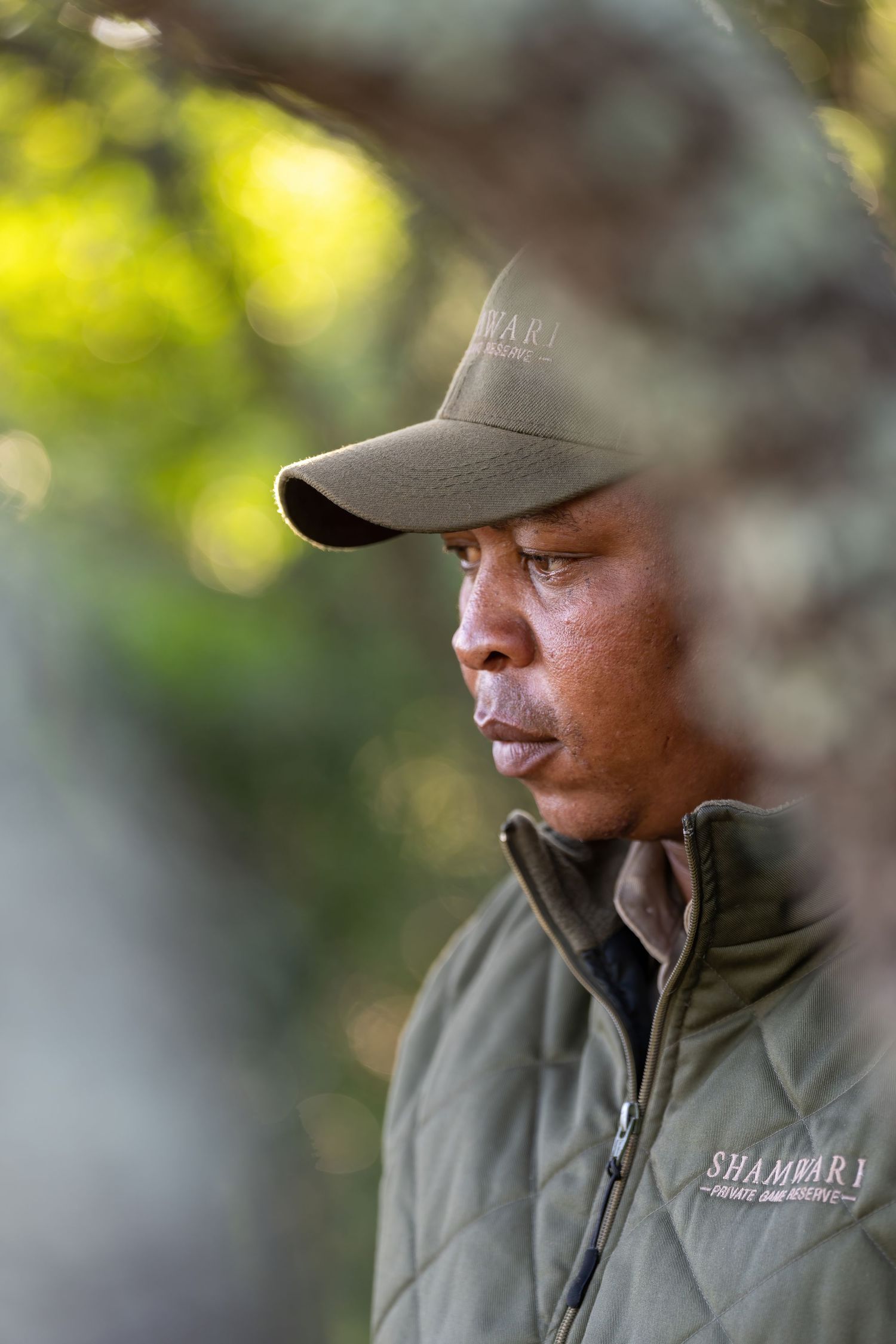 Professional wearing olive green jacket and baseball cap in an outdoor setting.
