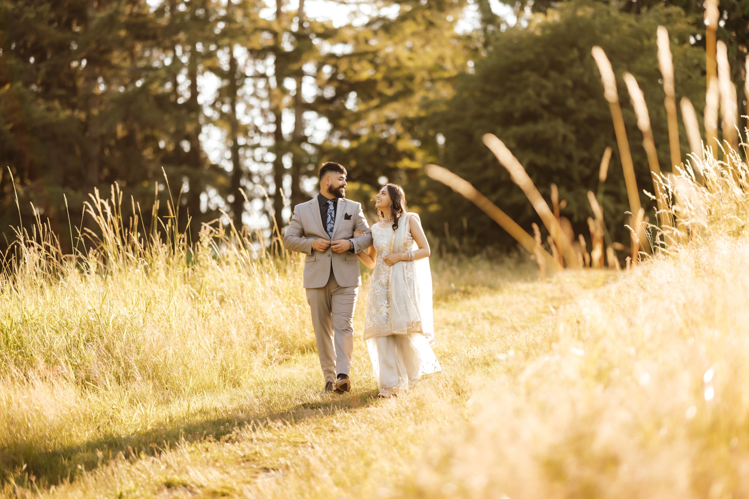 A couple walks together through golden grass at sunset.