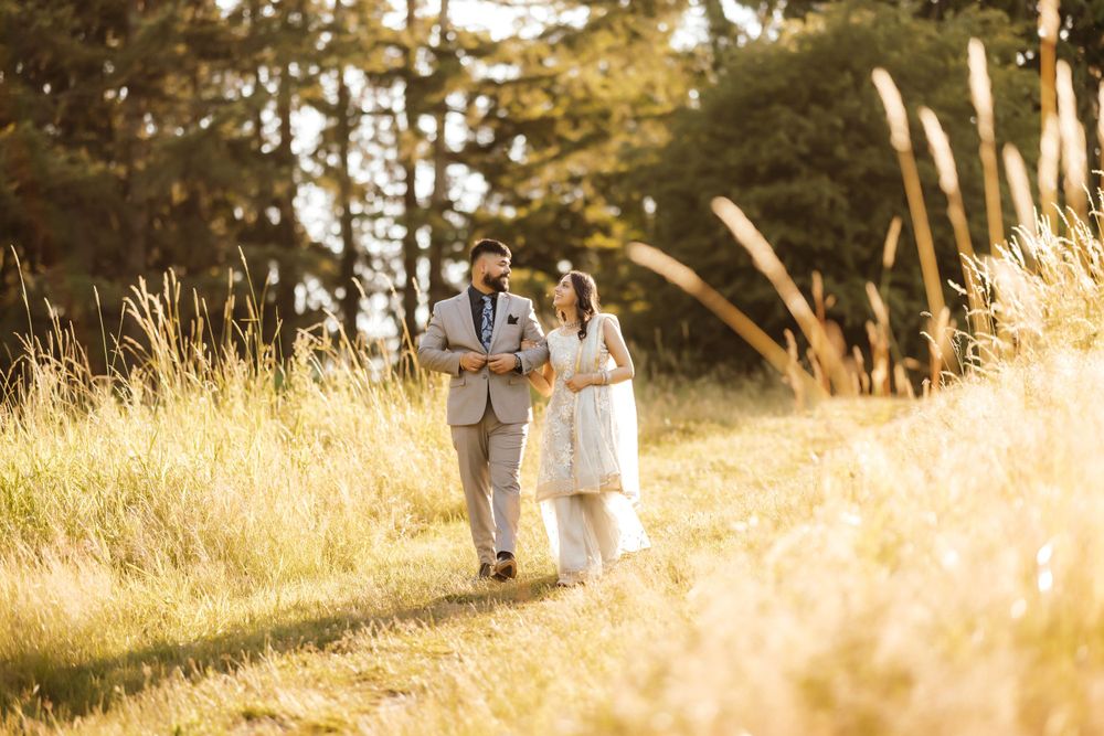 A couple walks together through golden grass at sunset.