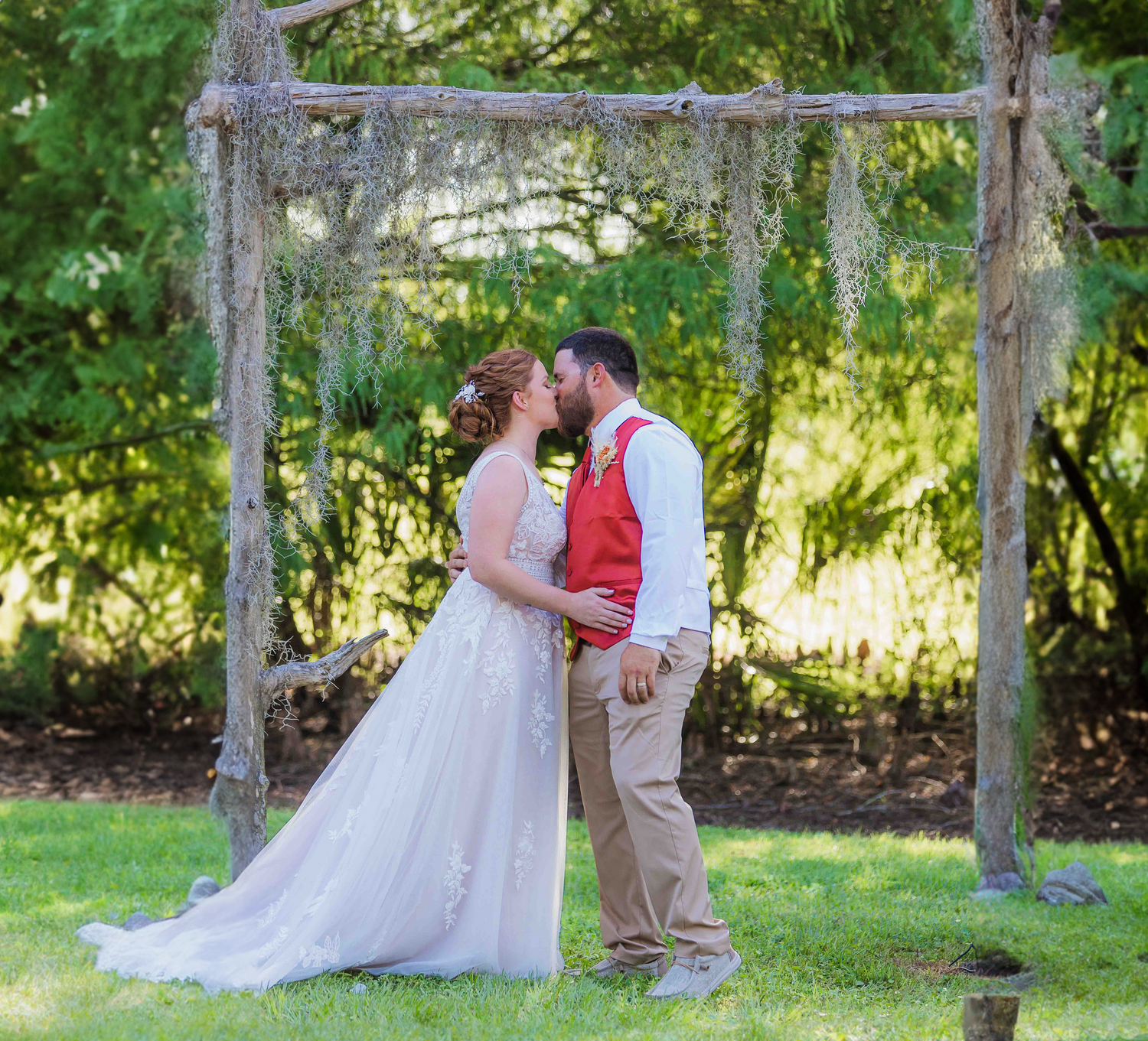 Rustic wooden wedding arch decorated with natural greenery in outdoor garden setting.