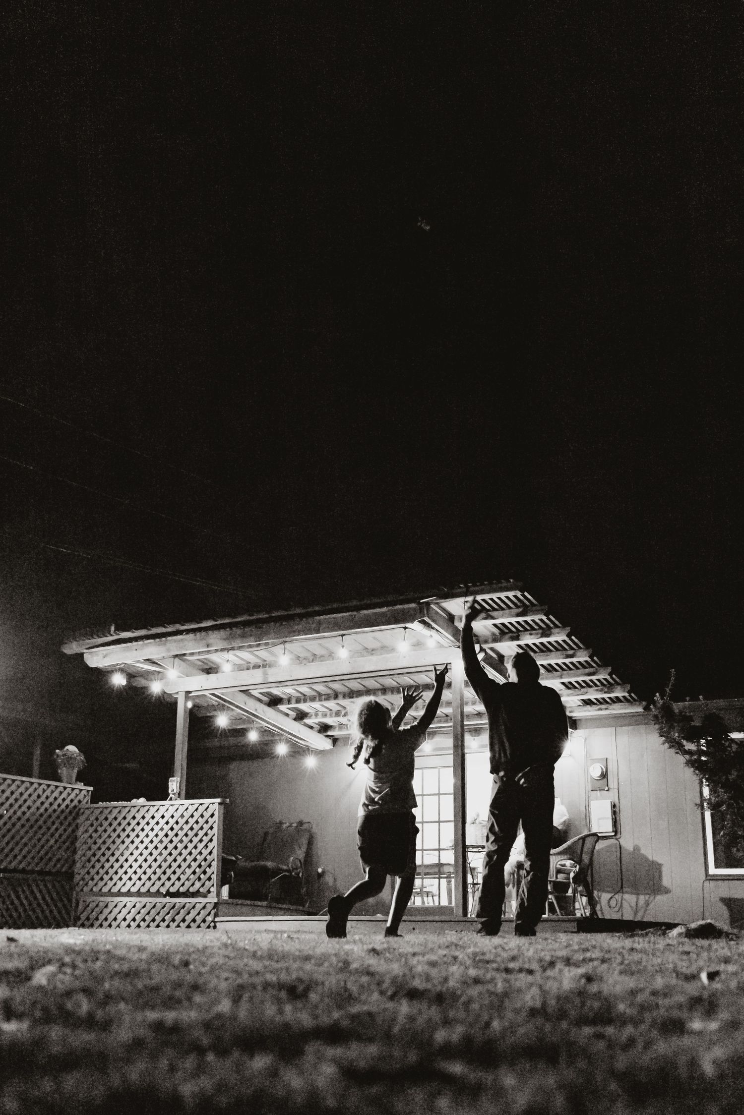 parent and child catching thrown toy in the backyard at night