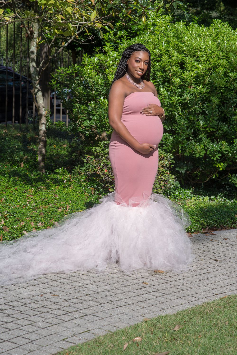 A person poses in a pink top and white tulle skirt on a stone pathway surrounded by greenery.