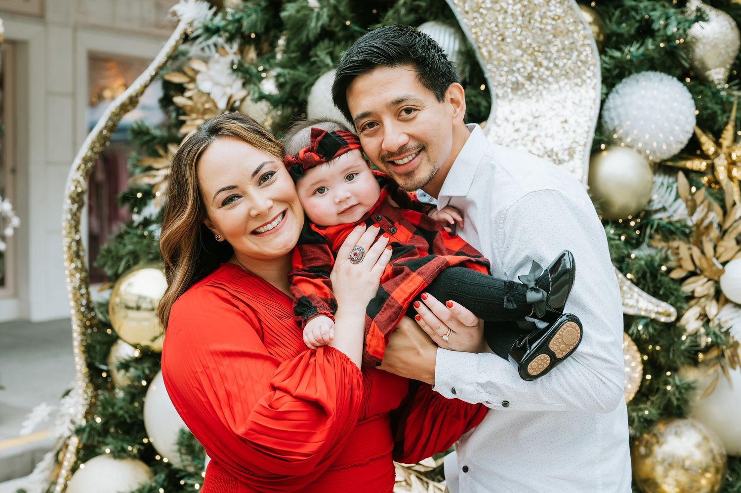 A happy family poses together in front of a decorated Christmas tree with gold and silver ornaments.