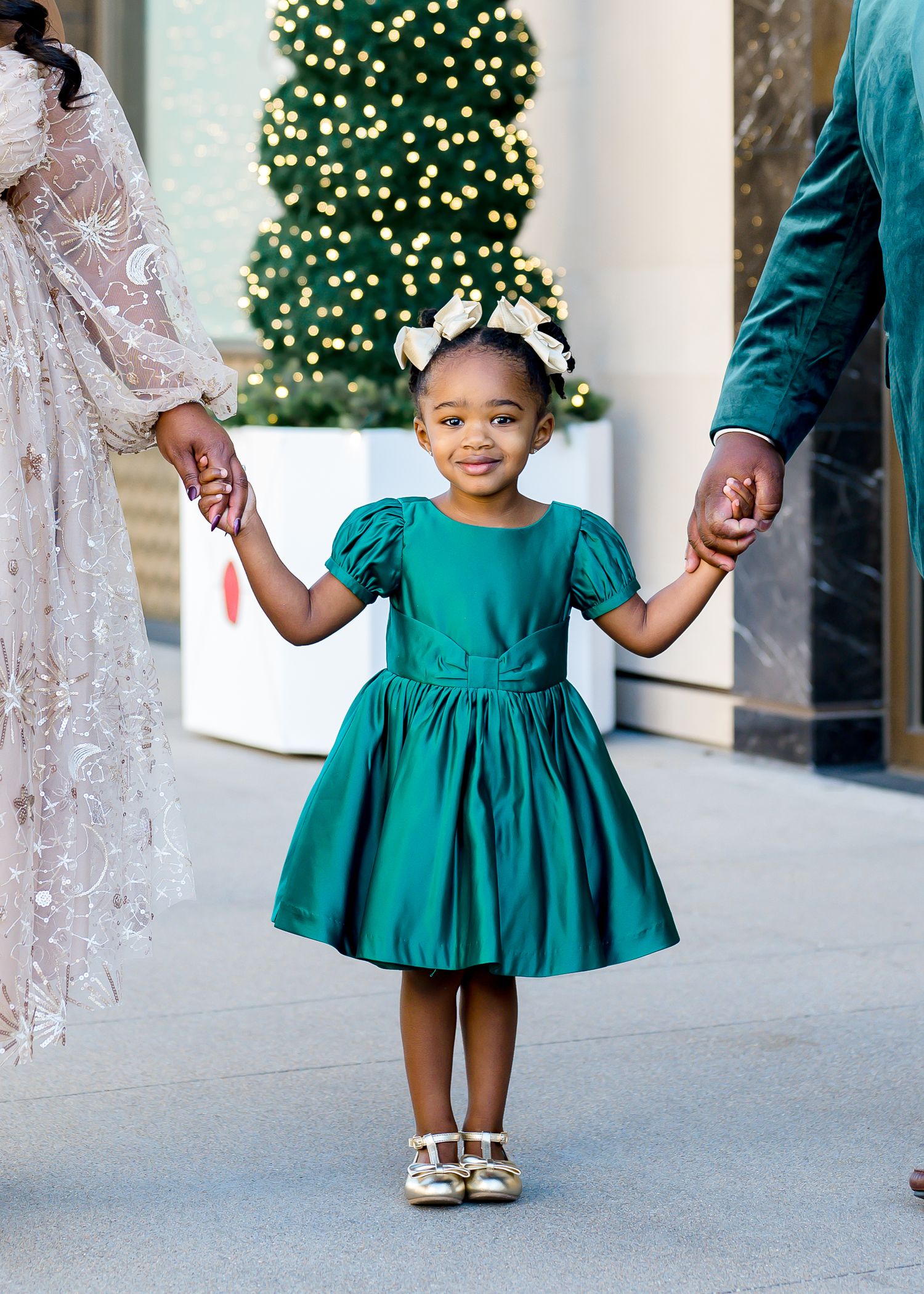 Holiday portraits featuring emerald green and white lace dresses against decorative storefront.