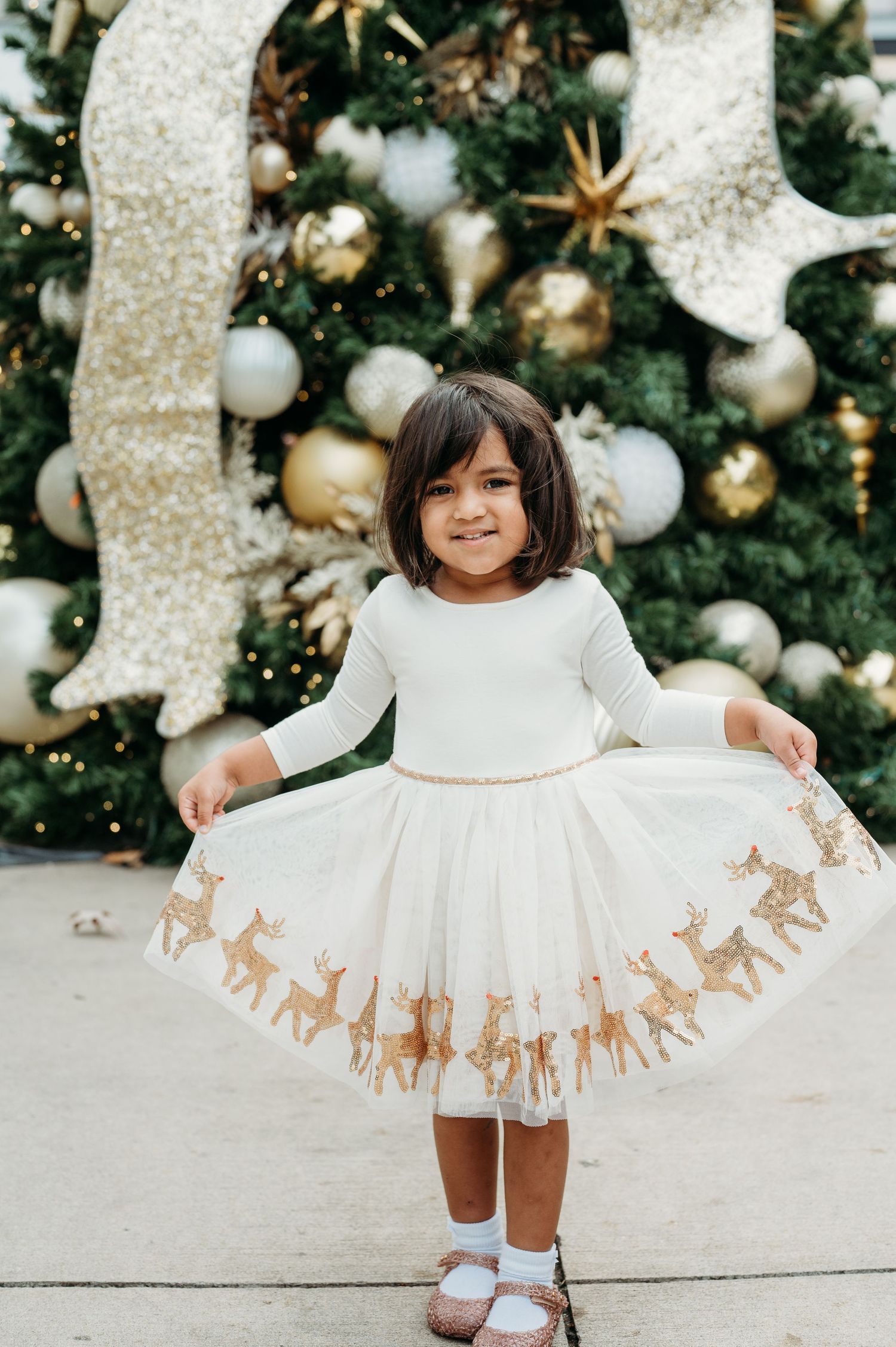 Festive white holiday dress with golden reindeer print displayed near decorated Christmas tree.