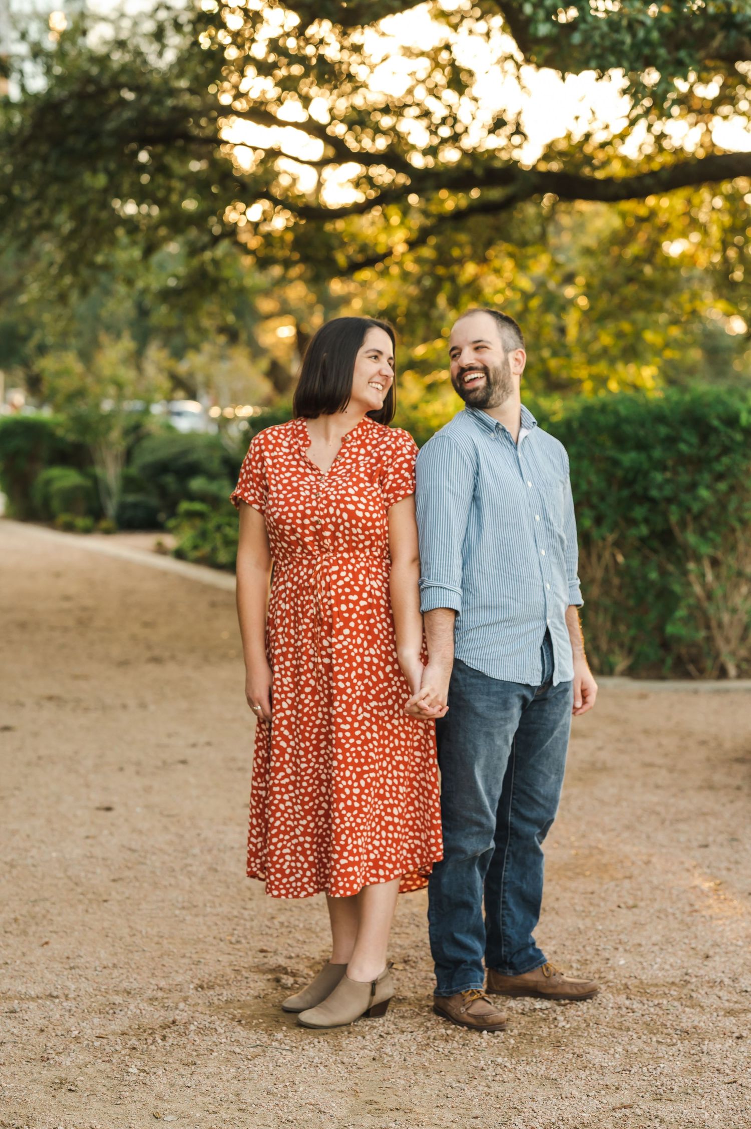 A couple in coordinating outfits shares a joyful moment together on a tree-lined path at golden hour.