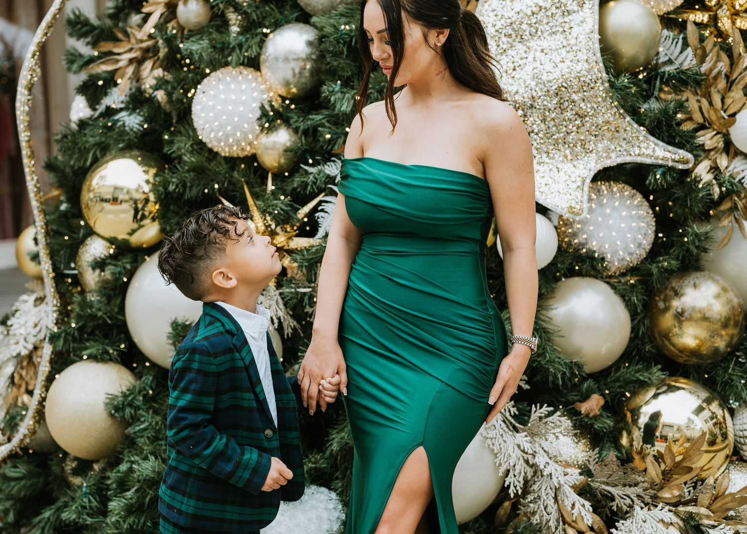 Women in elegant emerald green dresses pose near a festive Christmas tree with gold and silver ornaments.