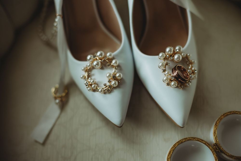 White bridal shoes with ornate pearl embellishments and wedding rings.