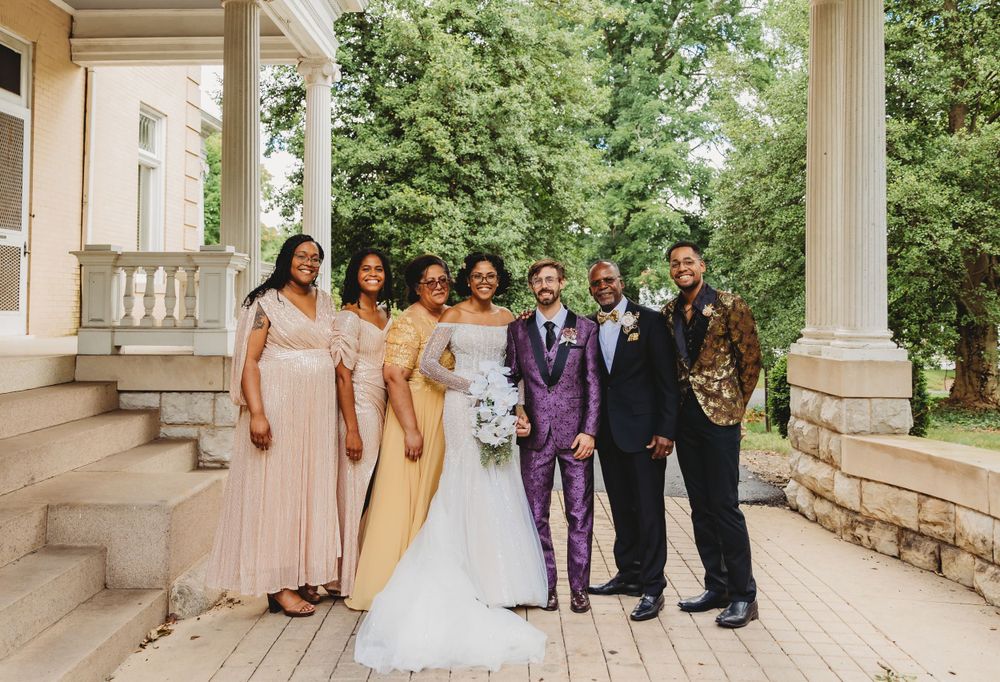 Wedding party poses on grand stone steps wearing coordinated formal attire in shades of yellow and purple.