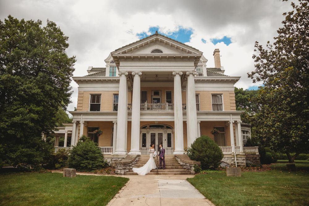 Majestic white colonial mansion with tall pillars and grand staircase entrance on a cloudy day.