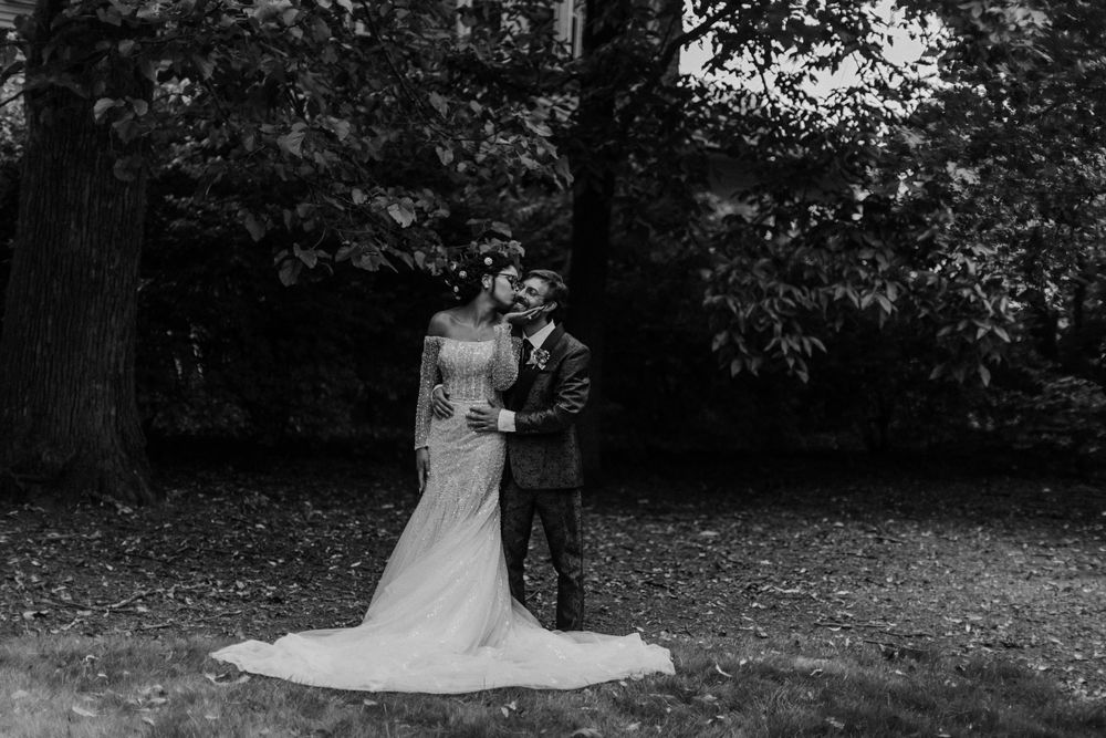 A black and white portrait of newlyweds embracing in a leafy outdoor setting.