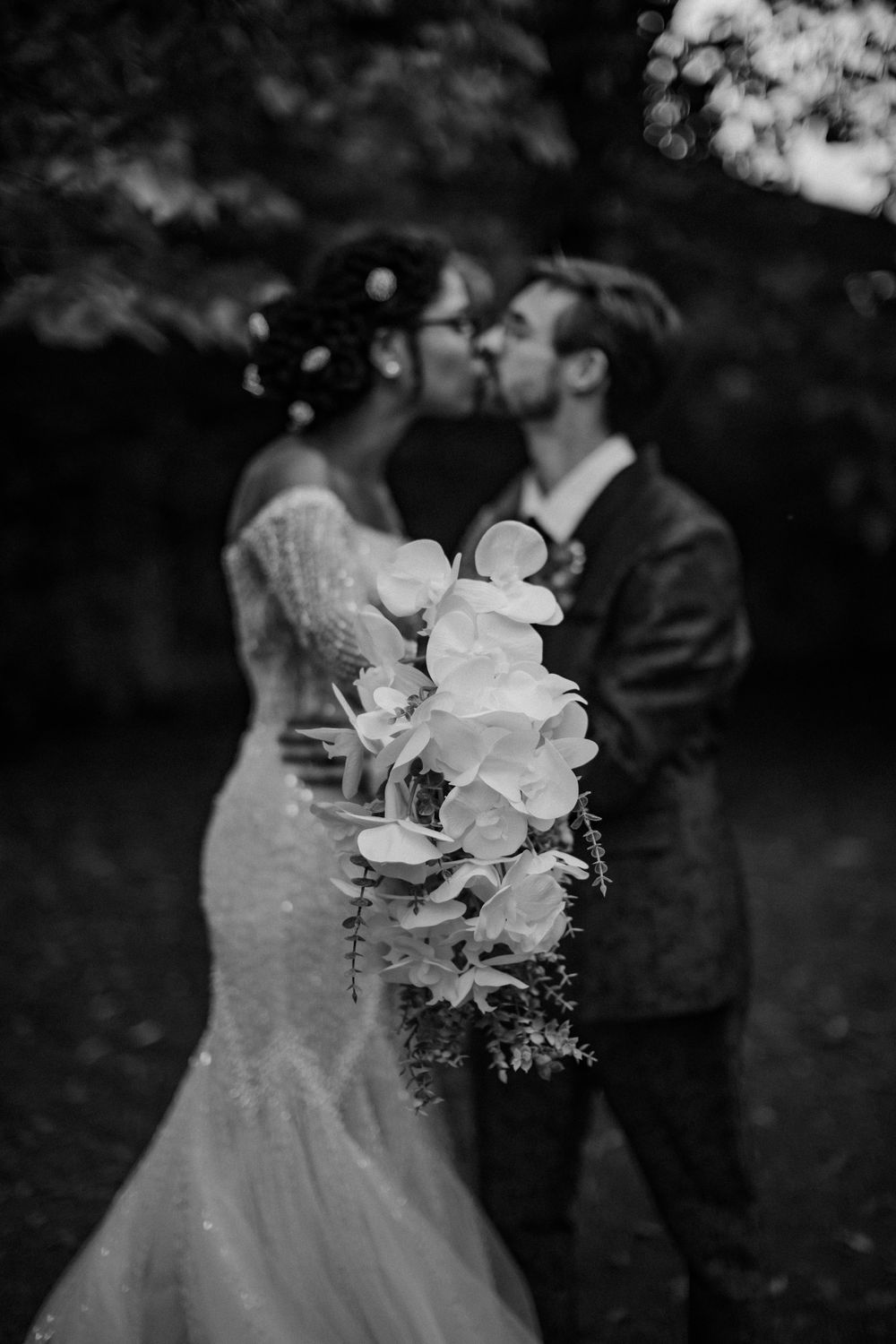 A romantic black and white shot of newlyweds kissing while holding a bouquet of white flowers.