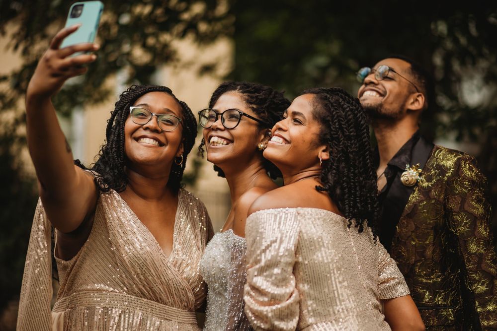 Bridesmaids in sparkly champagne dresses take a joyful selfie together during wedding celebrations.
