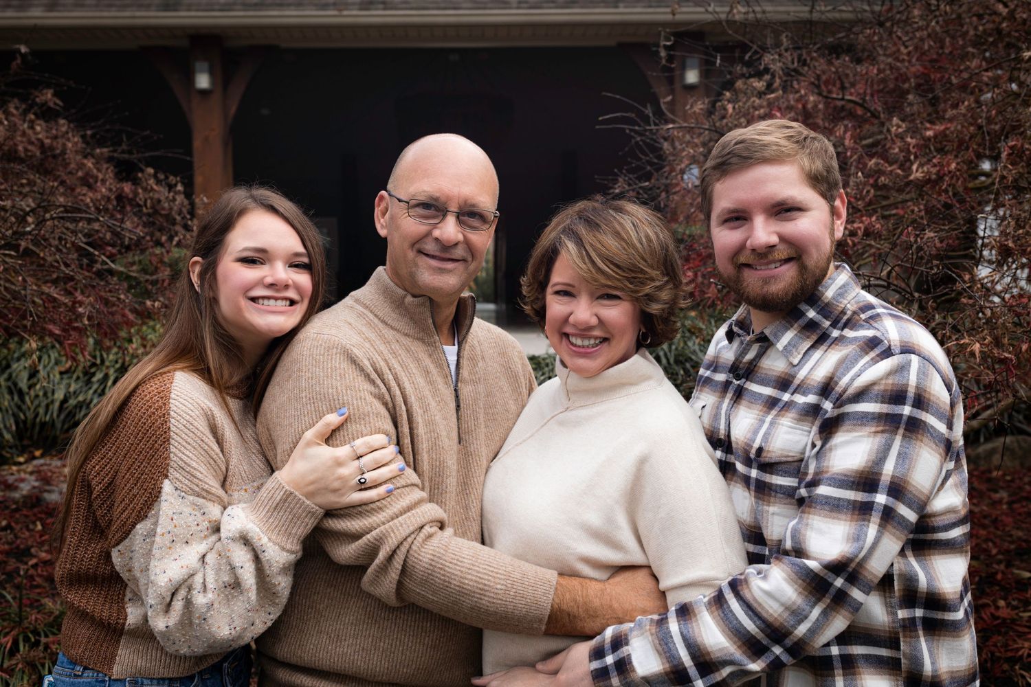Warm family portrait of four people in cozy sweaters against an autumn backdrop.