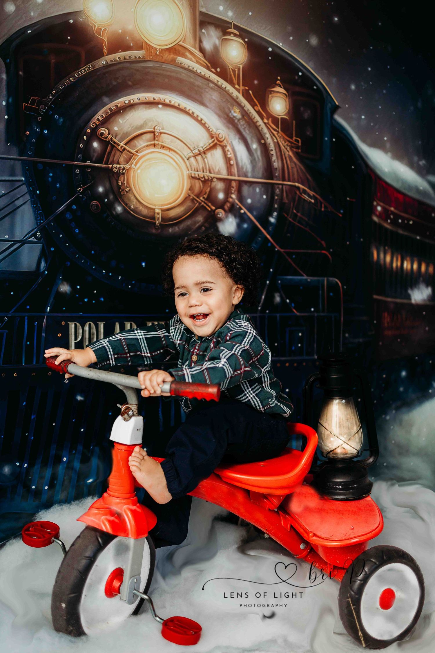 A child rides a red tricycle in front of a magical winter train backdrop.