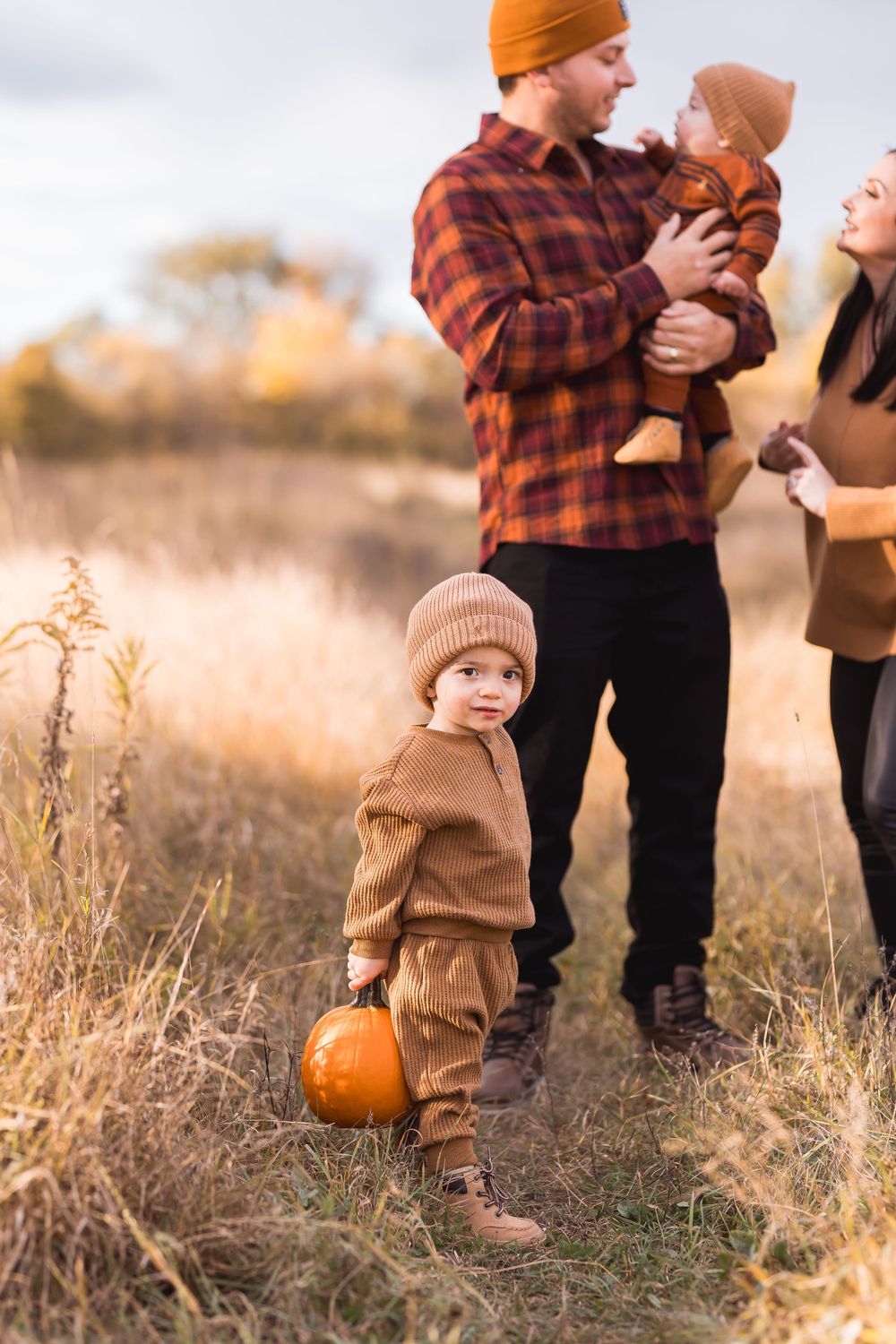 Young child holding pumpkin during autumn family photo session in golden field.
