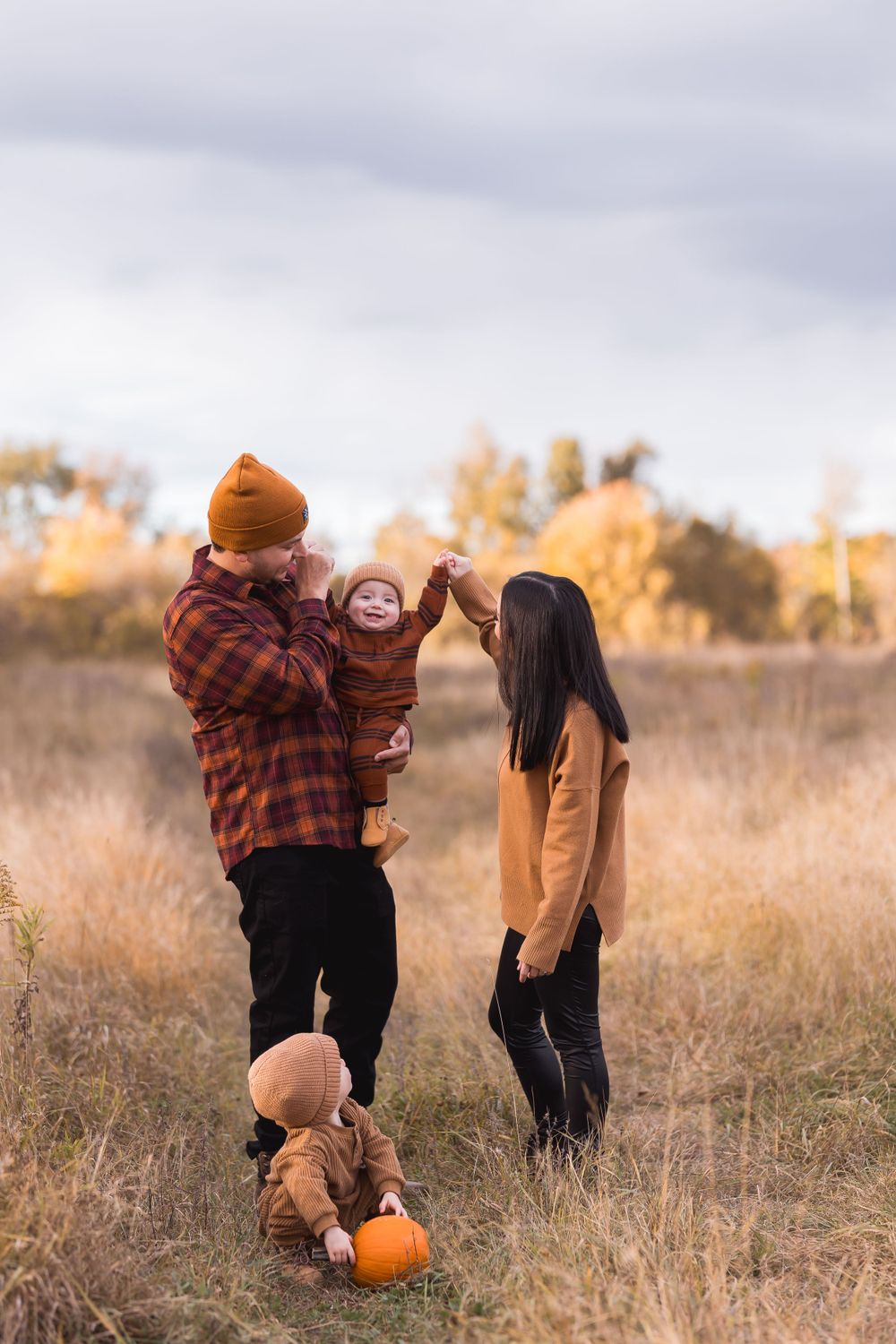 Family of four enjoying fall outdoor photoshoot in golden meadow with pumpkins.