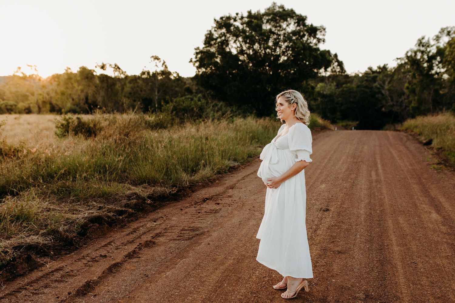 Romantic couple walking along a dirt road through golden fields at sunset.