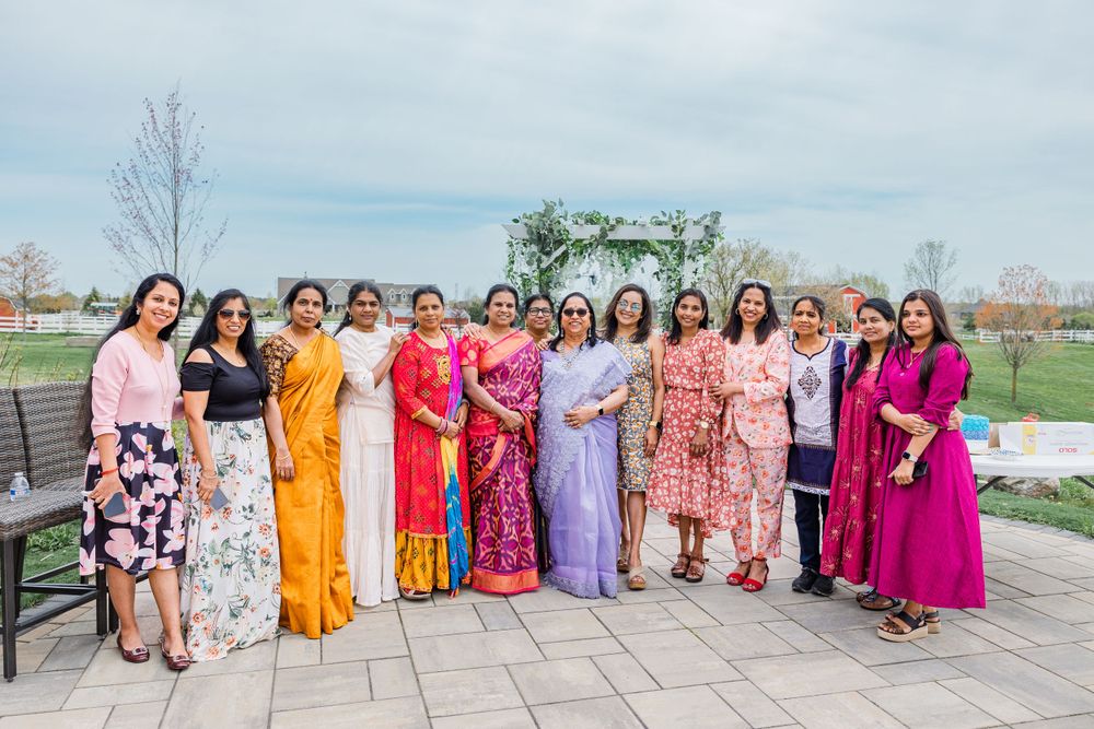 Group of women in colorful saris and dresses gather for a photo on a stone patio.
