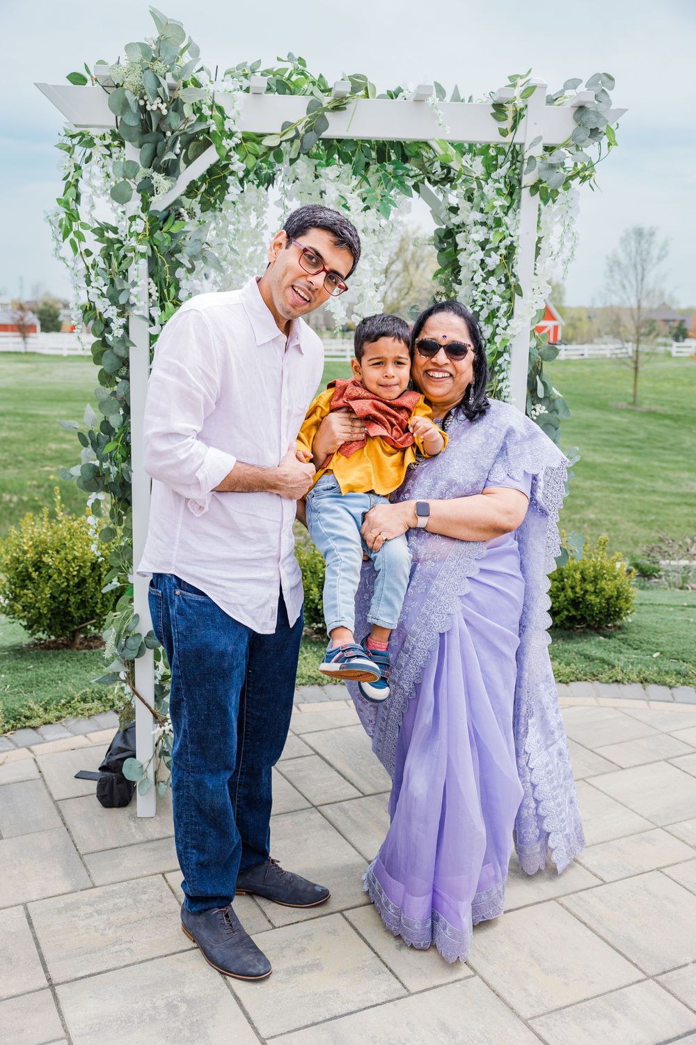 A family of three poses under a floral arch in a garden setting.