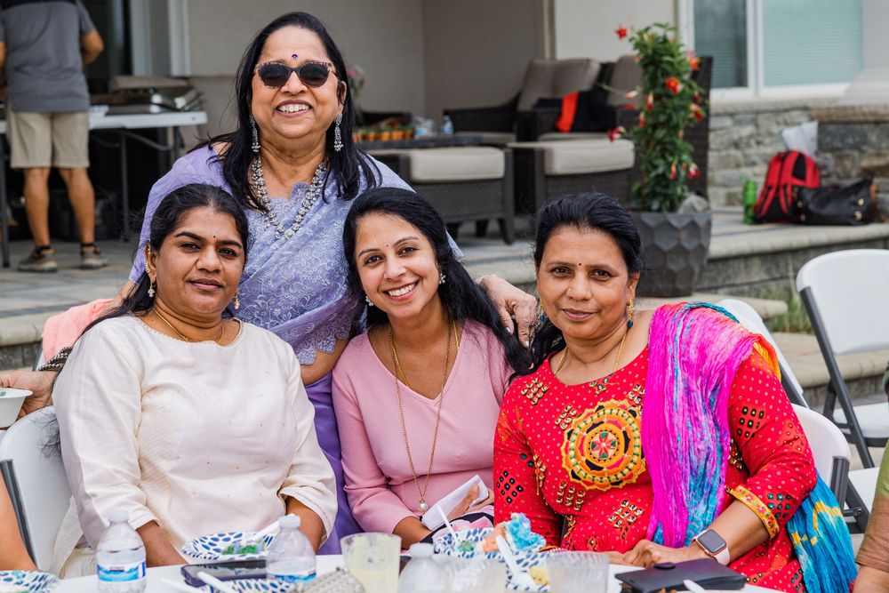 A group in colorful Indian attire poses together at an outdoor table during a celebration.