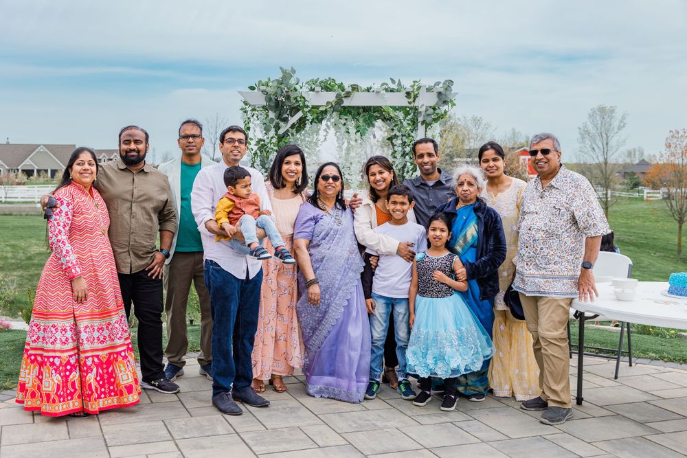 Large group in traditional Indian attire poses together outdoors under cloudy skies.