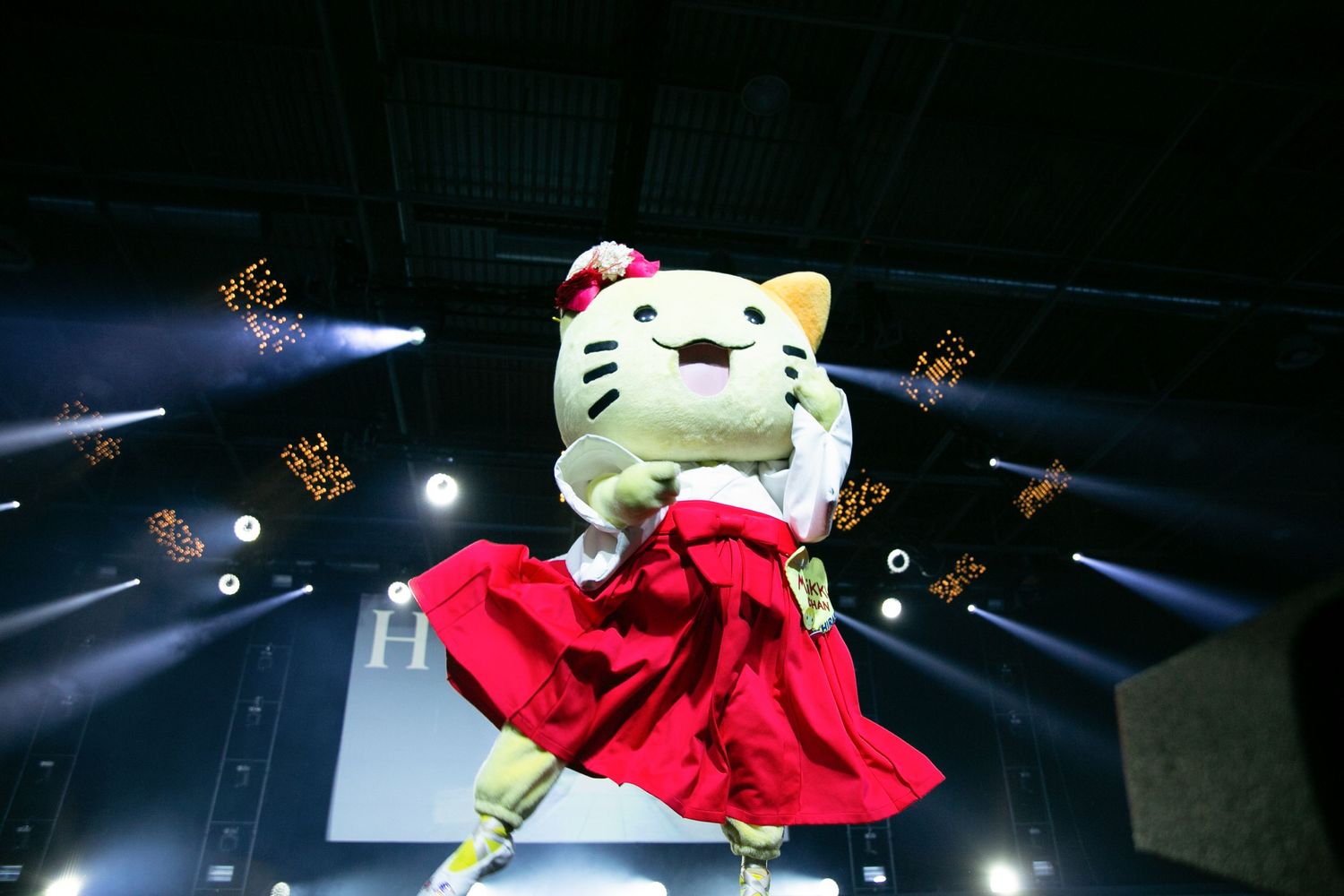 Hello Kitty mascot in red dress performing under spotlights at event stage.