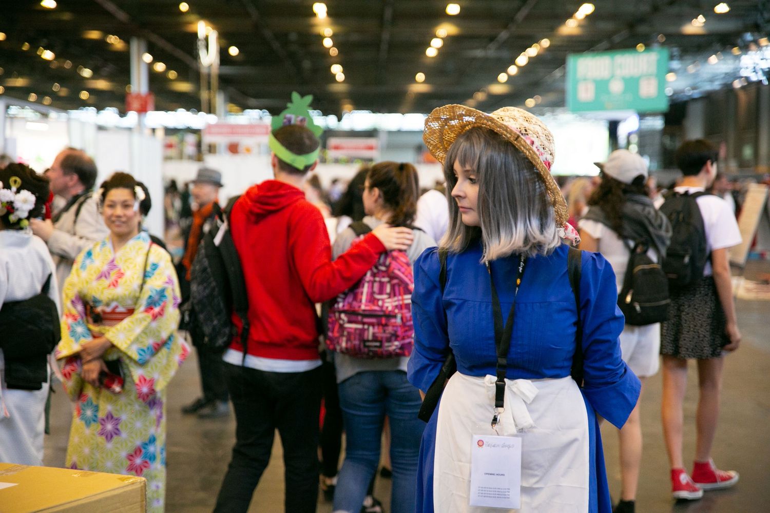 Crowd of convention attendees walking through indoor event space with some wearing traditional clothing.