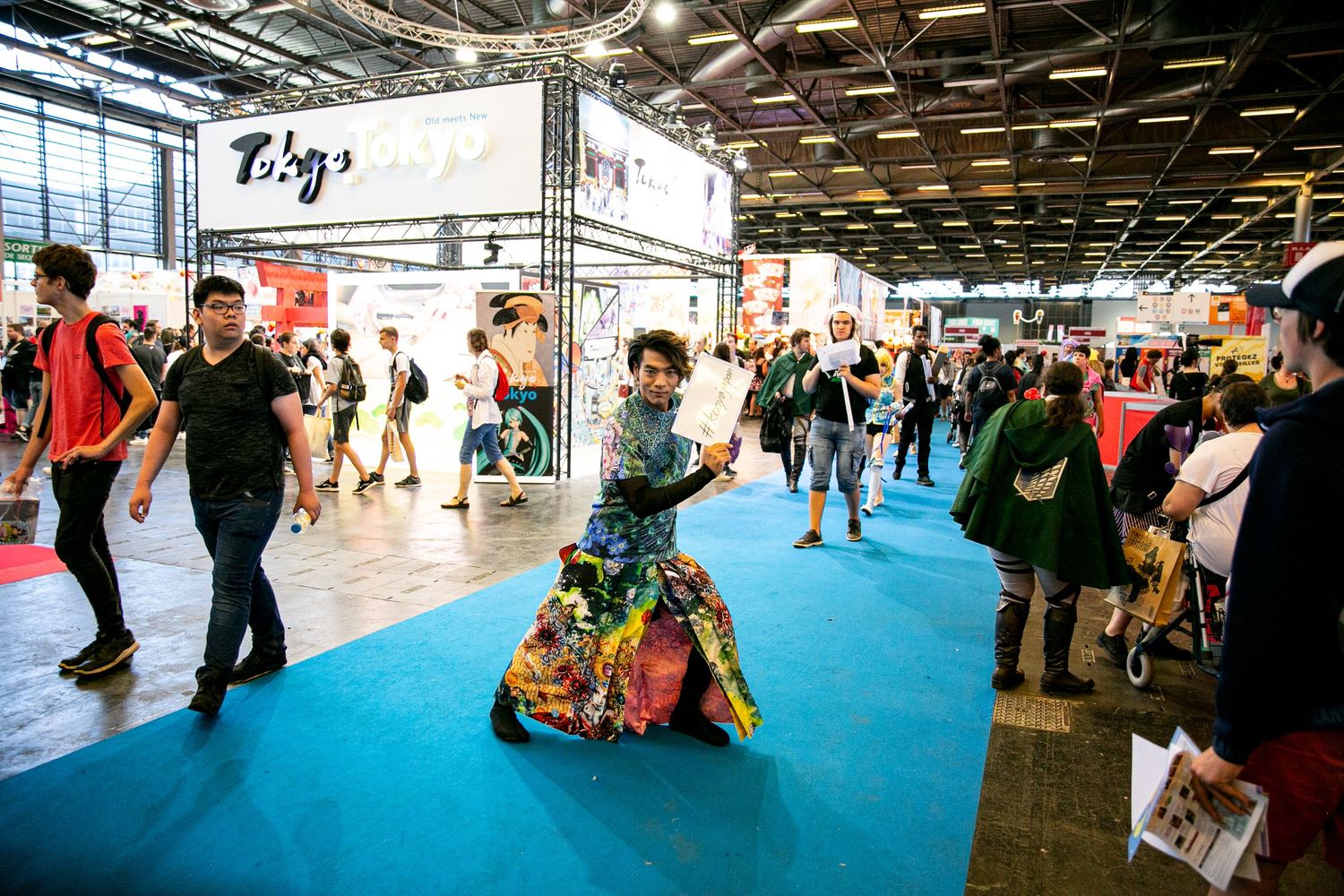 Cultural festival attendee in vibrant costume performing on blue floor at indoor convention.