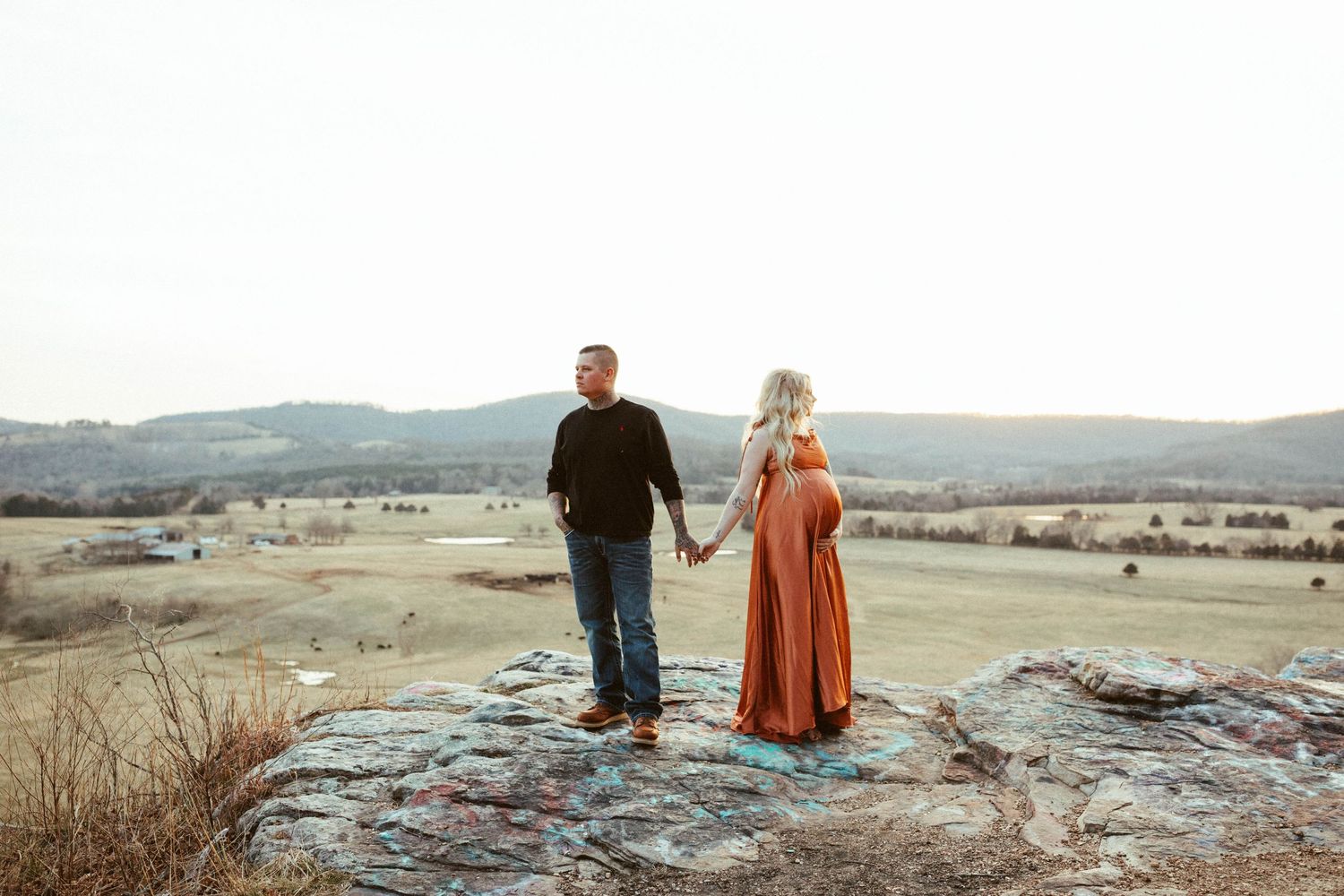 Couple standing together on rocky overlook with scenic countryside view.