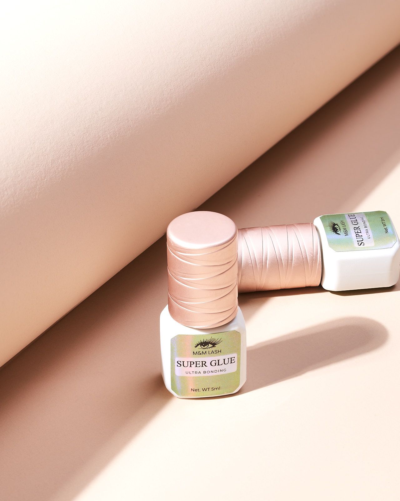 eye lash glue 1 standing 1 lying down on a beige background