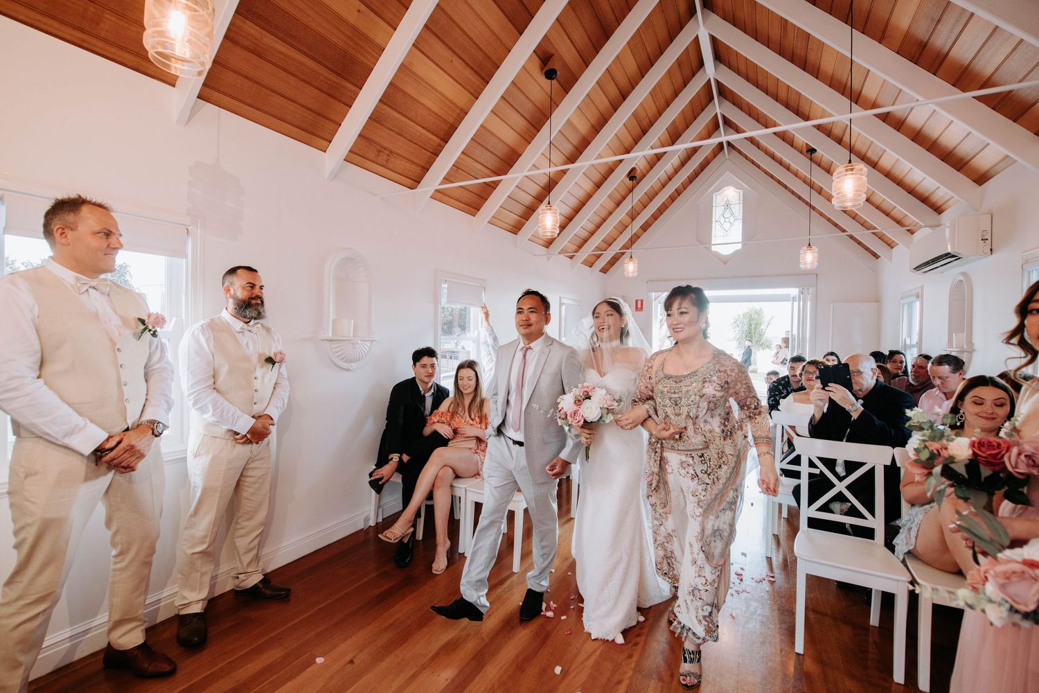 Wedding ceremony taking place in a bright chapel with wooden beams and white walls.