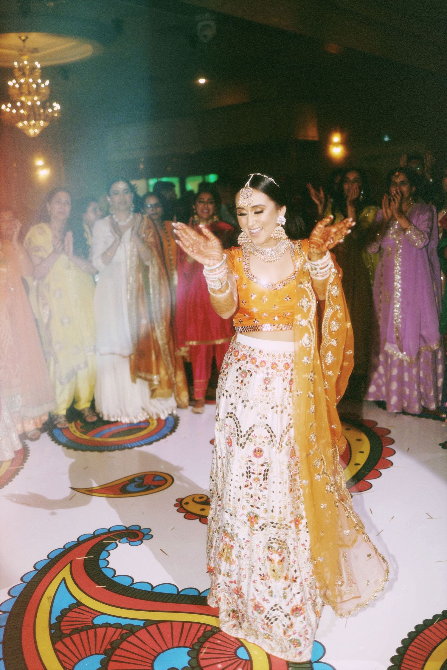 A bride in a gold and white lehenga dances during a wedding celebration on a decorated floor.