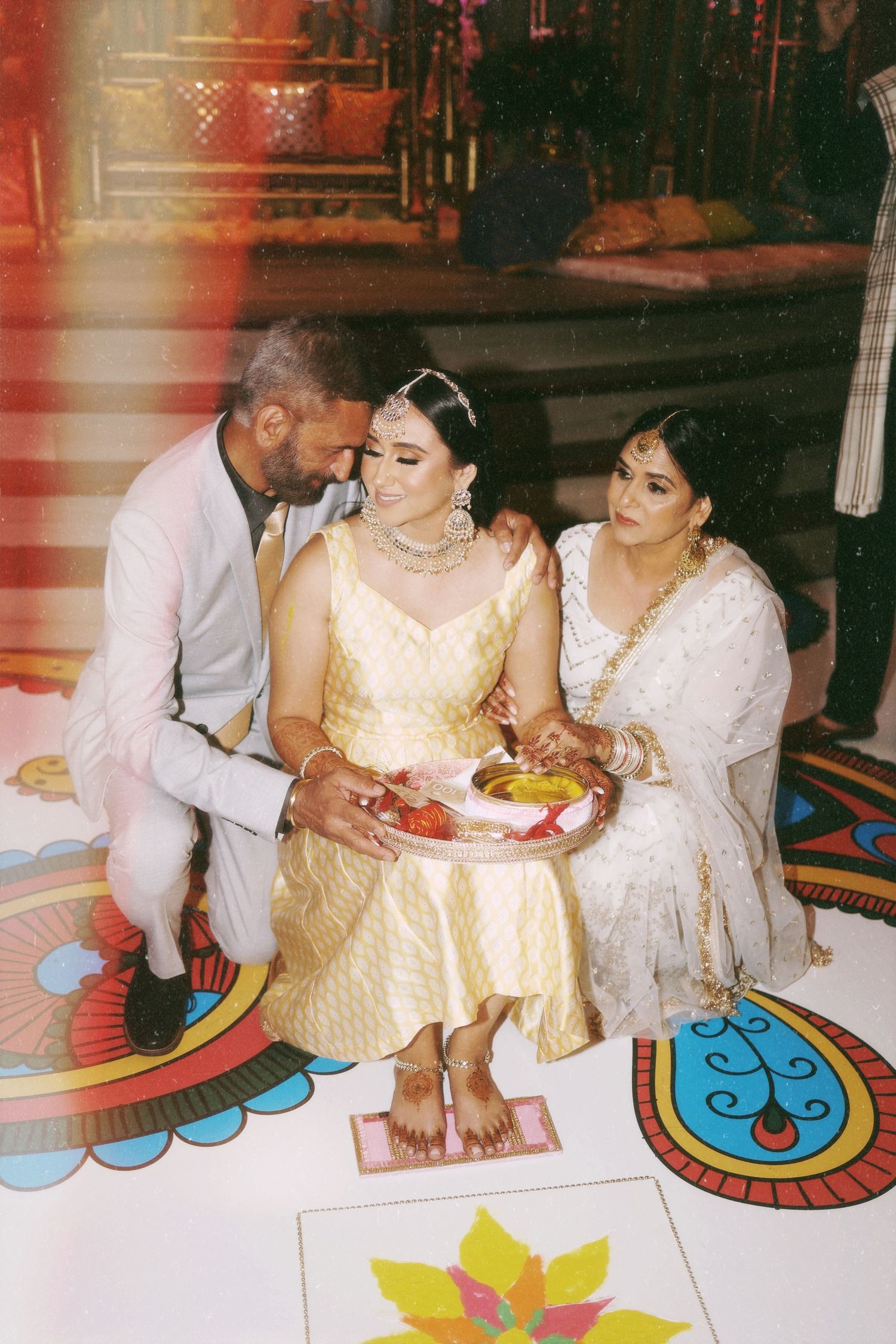 Three people gathered on a decorative floor during a traditional Indian ceremony.