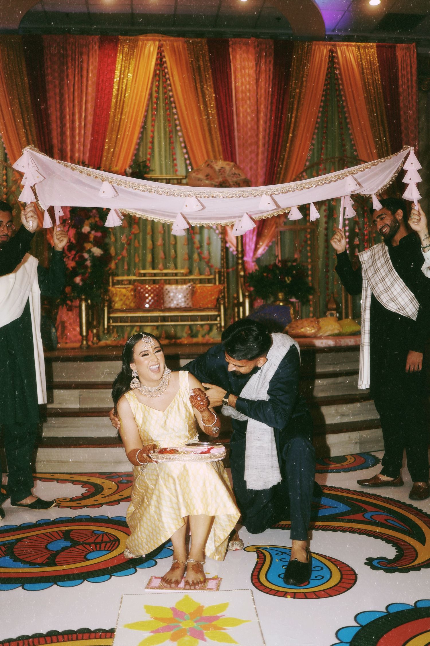Wedding ritual being performed under white canopy with colorful draped backdrop.