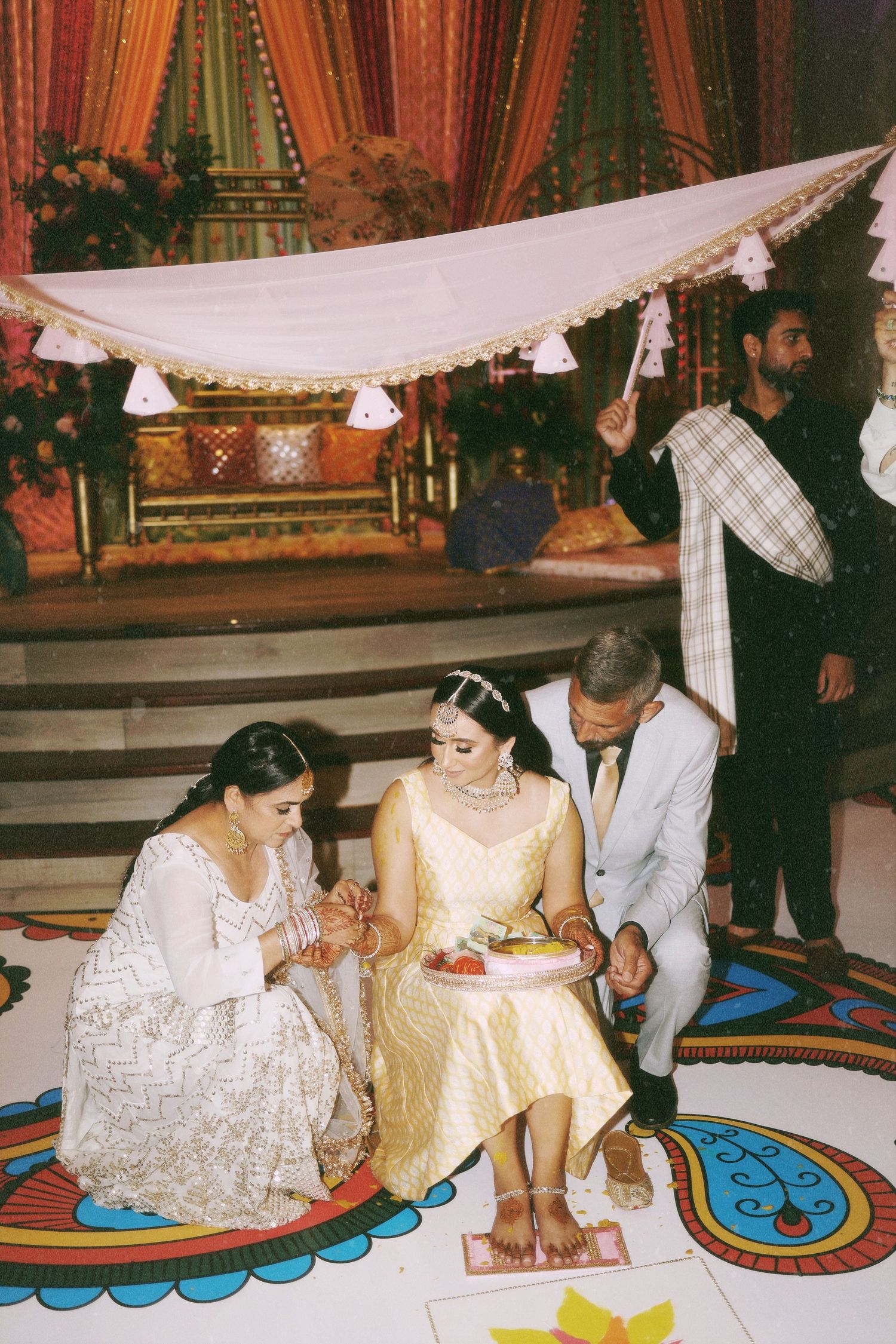 Traditional wedding ceremony under white canopy with detailed floor decorations.