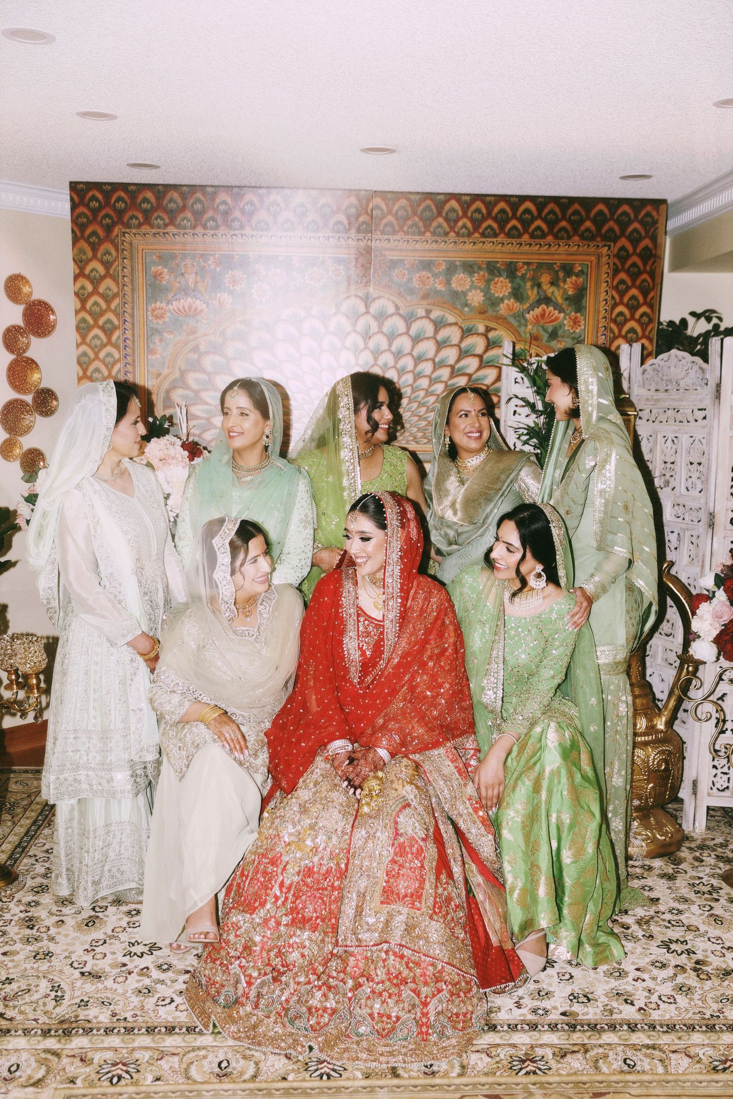 A group wearing traditional Indian attire gathers for a wedding photo against a patterned wall.
